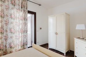 Ein Schlafzimmer mit Bett, Kleiderschrank, Schminktisch und einem Fenster mit Vorhängen.