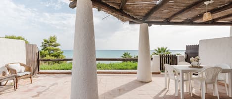 A covered patio with white chairs and a table, overlooking the sea.