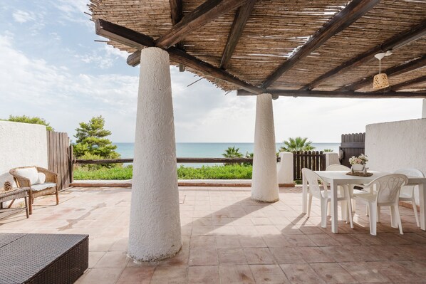 A covered patio with white chairs and a table, overlooking the sea.