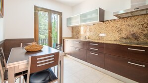 A modern kitchen with dark cabinets, a granite countertop, and a large window. - Holiday Home 'Nostra' with Mountain View, Private Pool and Wi-Fi (Cas Català)