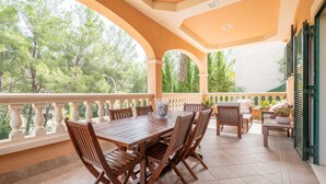 A covered outdoor patio with a wooden table and chairs, surrounded by a balustrade, and overlooking a garden. - Holiday Home 'Nostra' with Mountain View, Private Pool and Wi-Fi (Cas Català)