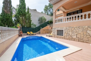 A swimming pool with lounge chairs, a stone wall, and a balcony with a railing.