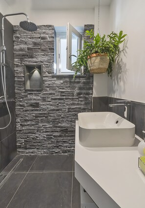Une salle de bain moderne avec un mur en pierre, une grande baignoire, une plante suspendue et une douche.