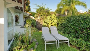 En have med to liggestole, en stenvæg og mange forskellige planter.