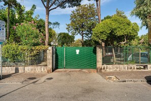 A gated entrance with a green gate, a stone wall, and a paved path leading to a building.