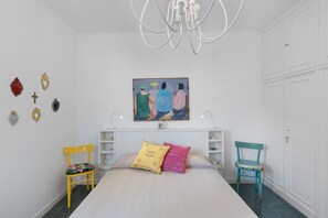 A bedroom with a bed, two chairs, a painting, and a chandelier.