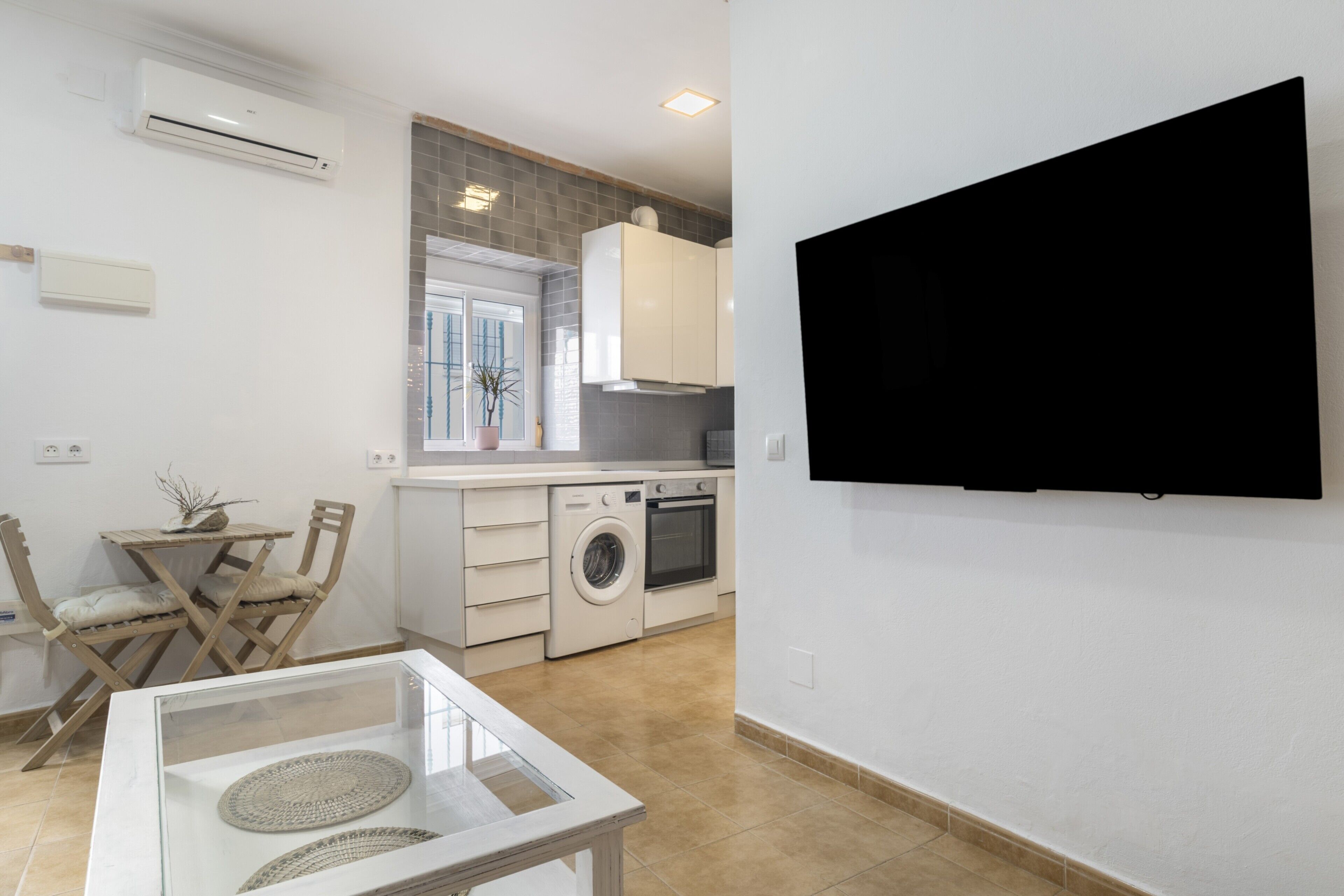 Eine moderne Küche mit Waschmaschine, einem Essbereich mit Stühlen und einem an der Wand montierten Fernseher.