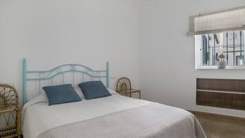 Un dormitorio con cama, dos almohadas, cabecera, ventana y estante.