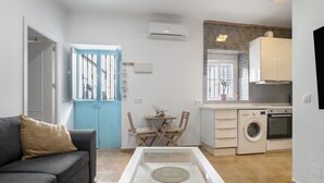 Een compact woongedeelte met een bank, een salontafel, een eettafel met stoelen, een wasmachine en een keukenhoek.