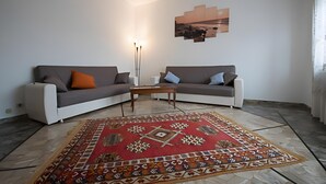 A living room with two sofas, a coffee table, a patterned rug, and a wall-mounted artwork. - Apartment 'Serravalle Shopping' with Balcony and Wi-Fi (Serravalle Scrivia)