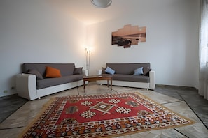 Un soggiorno con due divani, un tavolino da caffè, un tappeto decorato e un'opera d'arte appesa al muro.