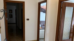 A hallway with stone flooring, wooden doors, and a metal rack. - Apartment 'Serravalle Shopping' with Balcony and Wi-Fi (Serravalle Scrivia)