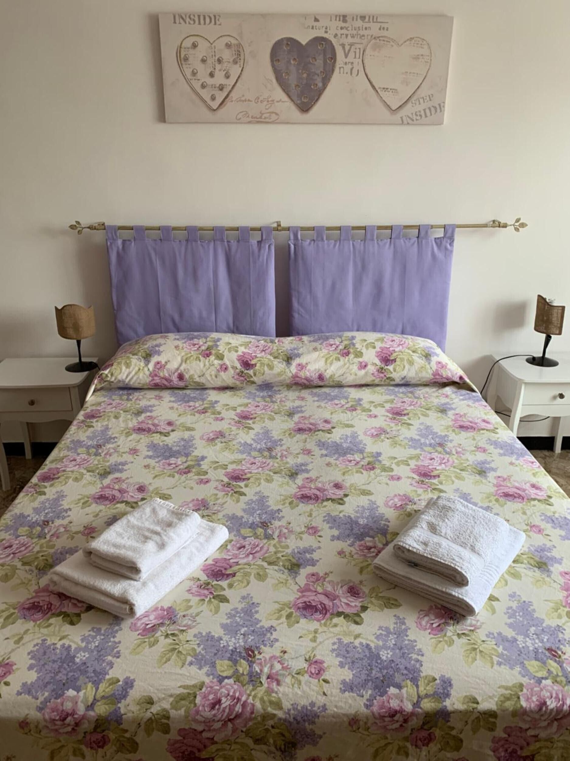 Un letto con biancheria da letto floreale, due comodini e una parete decorata con cuori.