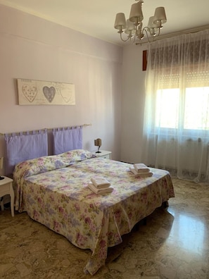 Una camera da letto con un letto, un comodino, un lampadario, una finestra con tende e un addobbo a parete.