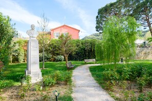 Une statue dans un jardin, avec un sentier, des bancs et un bâtiment en arrière-plan.