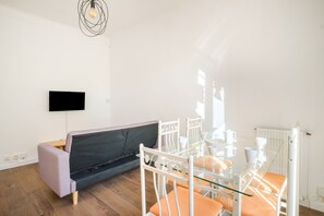 Un salon moderne comprenant un canapé, une table à manger en verre, des chaises, un téléviseur à écran plat et un radiateur.