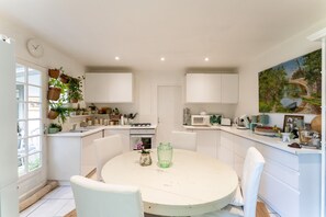 A modern kitchen with white cabinets, a round dining table, and hanging plants. - Holiday Home 'En Bord De Sorgue' with Private Pool, Private Terrace and Wi-Fi (Châteauneuf-de-Gadagne)