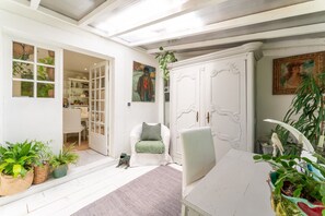A room with a white door, a chair with a cushion, a table, and potted plants.