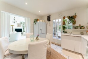 A modern kitchen with white cabinetry, a dining area with a round table, and a living space with a TV and white furniture.