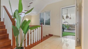 Una escalera con barandillas de madera y una planta en maceta, que lleva a una habitación con vistas a un balcón y zona exterior.