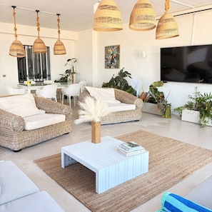 Un salón moderno con muebles de mimbre, una mesa de centro blanca y un televisor de pantalla plana grande.