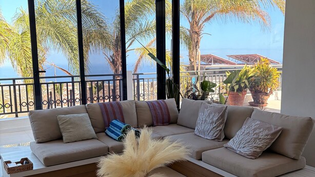 Una sala de estar moderna con un sofá grande, una mesa de centro y vistas a palmeras y al mar.