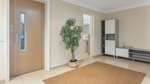 Un pasillo con una puerta color beige, una planta en maceta, un armario blanco y un suelo de baldosas.
