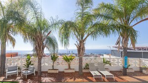 Un área de piscina en la azotea con sillones de descanso, palmeras y vista al océano.