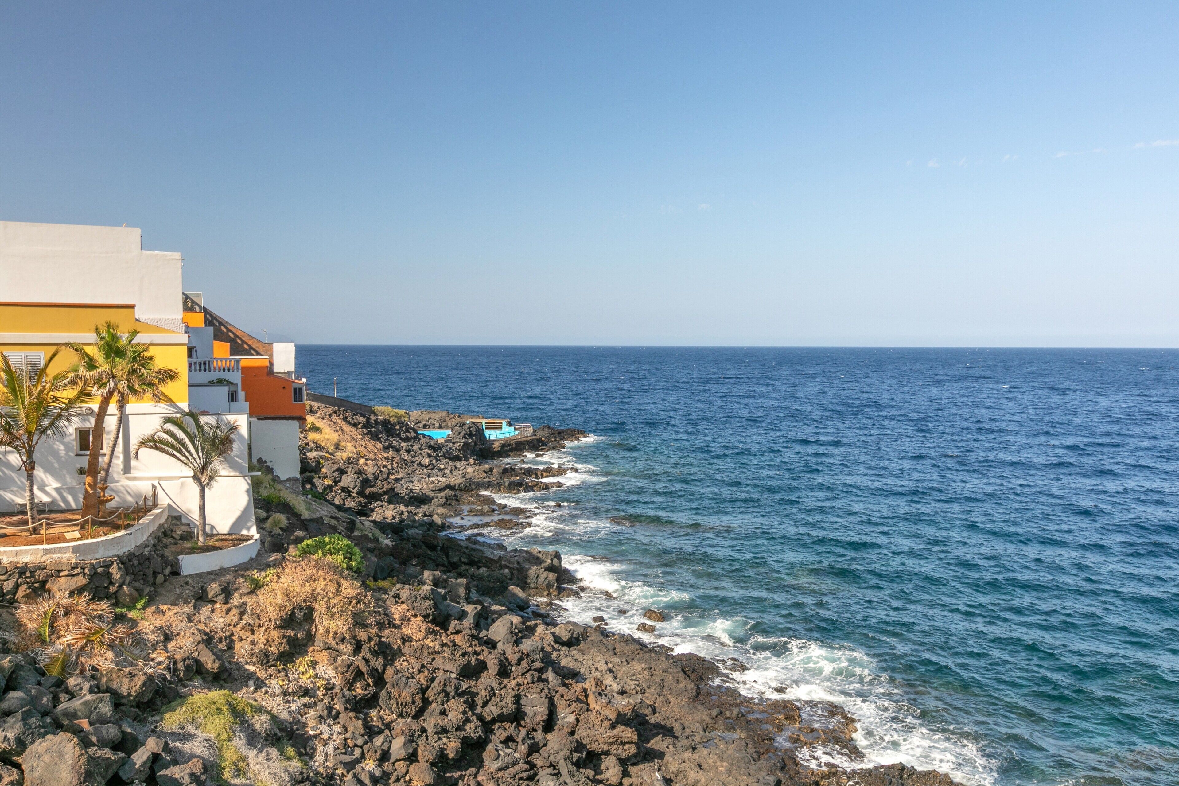 A coastal building with a rocky shoreline, a clear view of the ocean, and a small pool area.
