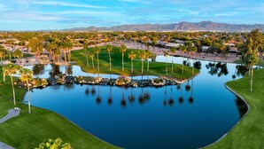 A golf course with a large pond, palm trees, and a mountainous backdrop. - Pebble Creek  2-bedroom plus office/bedroom. Fenced backyard. (Goodyear)
