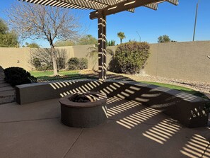 Relax by the fire pit in a serene outdoor space surrounded by lush greenery and a pergola.