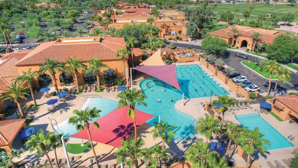 A resort with multiple swimming pools, palm trees, and a parking area. - Pebble Creek  2-bedroom plus office/bedroom. Fenced backyard. (Goodyear)
