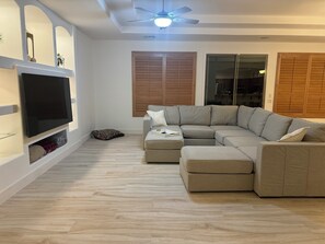 Relax in this spacious living room with a large L-shaped sofa, flat-screen TV, and ceiling fan.
