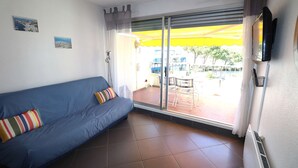 Ein Zimmer mit einem blauen Sofa, einer Glasschiebetür zu einem Außenbereich und einem wandmontierten Flachbildfernseher.