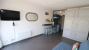 Ein kleiner Wohnraum mit Fernseher, Küchenzeile und Kleiderschrank.