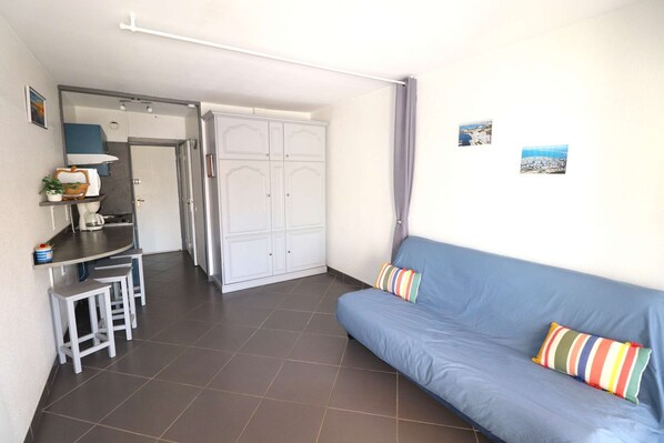 A room with a blue sofa, two stools, a white wardrobe, and a small table with a plant.