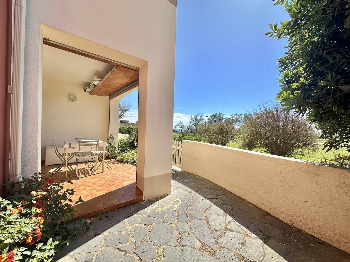 A patio with a table and chairs, a small garden area, and a view of the surrounding landscape.