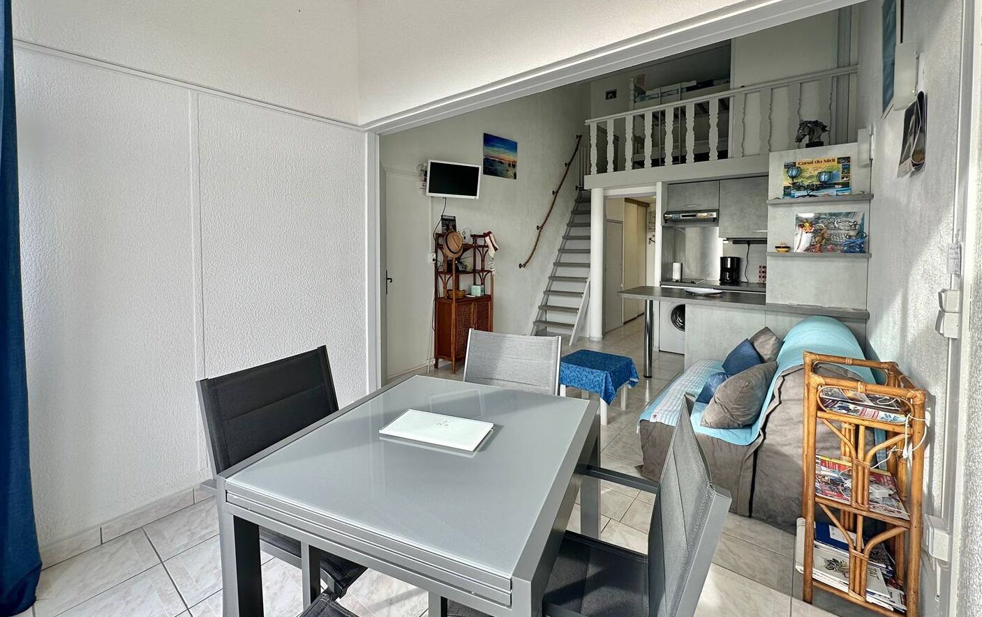 Un espacio habitable compacto con comedor, kitchenette y una escalera que lleva a un nivel superior.