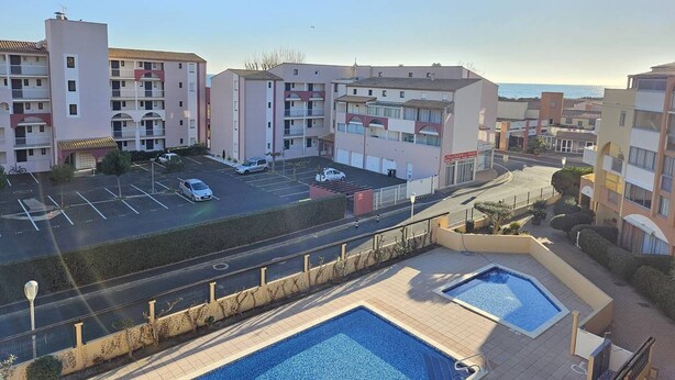 A residential building with multiple balconies, a parking lot, and a swimming pool area.