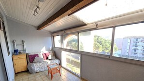 A room with a large window, a sofa, a wooden cabinet, and a small orange chair.