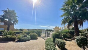 Ein sonniger Innenhof mit Palmen, einem Metallgitter und einem Gebäude im Hintergrund.