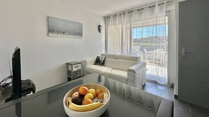 Ein modernes Wohnzimmer mit einem Glastisch, einem weißen Sofa, einem Gemälde an der Wand und Blick durch große Fenster.