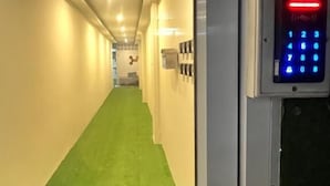 Un pasillo con alfombra verde, un teclado de seguridad en la pared y una puerta al final.