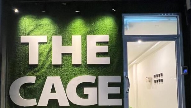 Entrada de un hotel con una pared de césped artificial verde y las palabras 'THE CAGE' en letras grandes.
