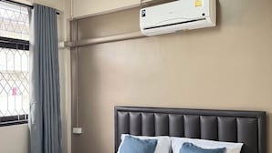 Una habitación de hotel con cama, ventana con cortinas, aire acondicionado y toallas sobre la cama.