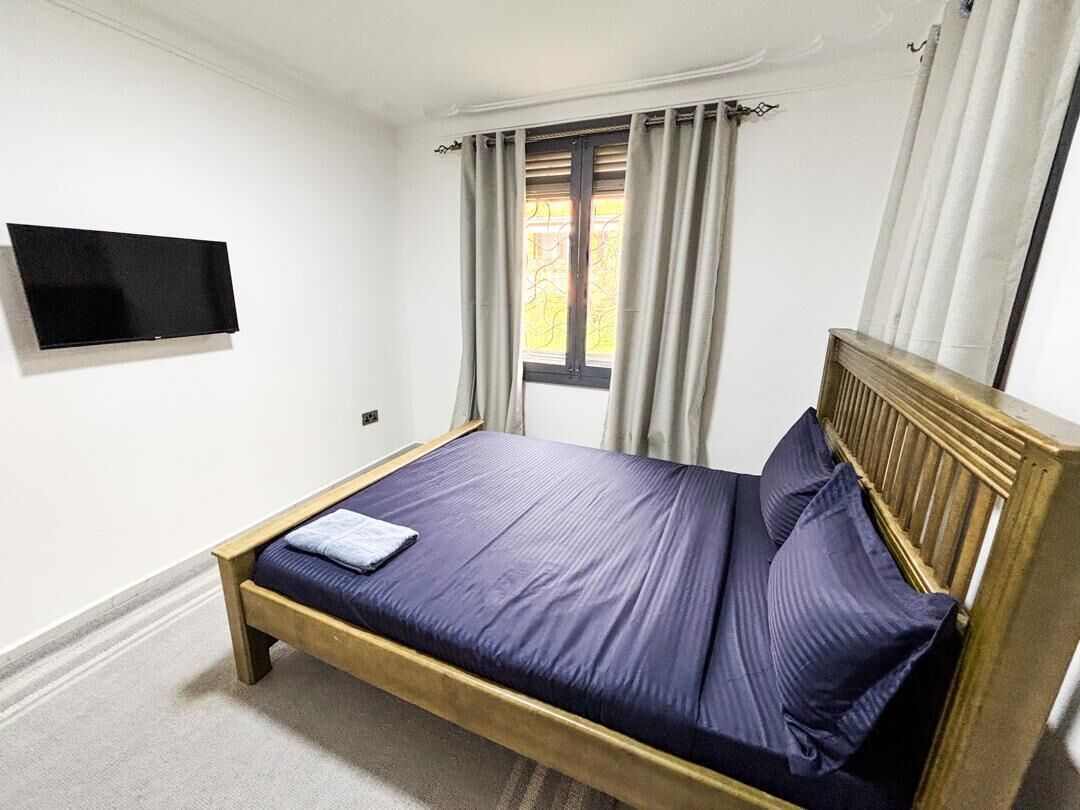 A bedroom with a bed, a television mounted on the wall, and a window with curtains.