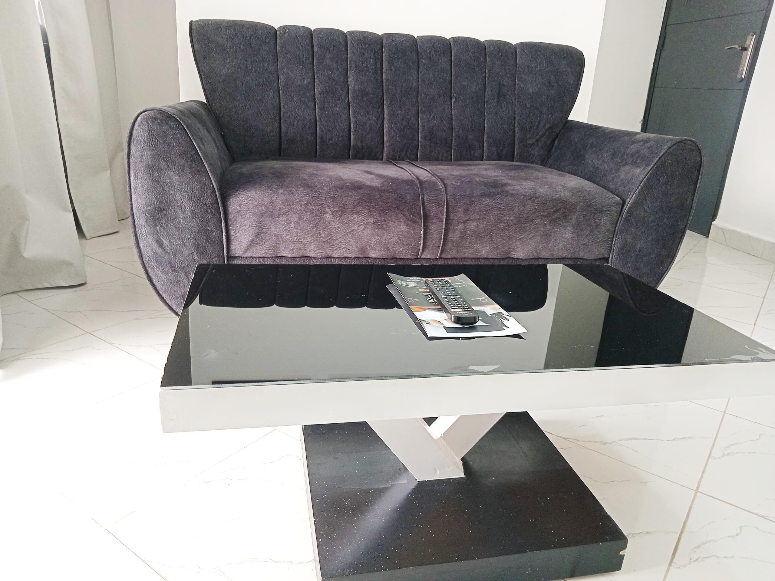 A modern living room with a dark grey sofa, a glass coffee table, and a remote control on the table.