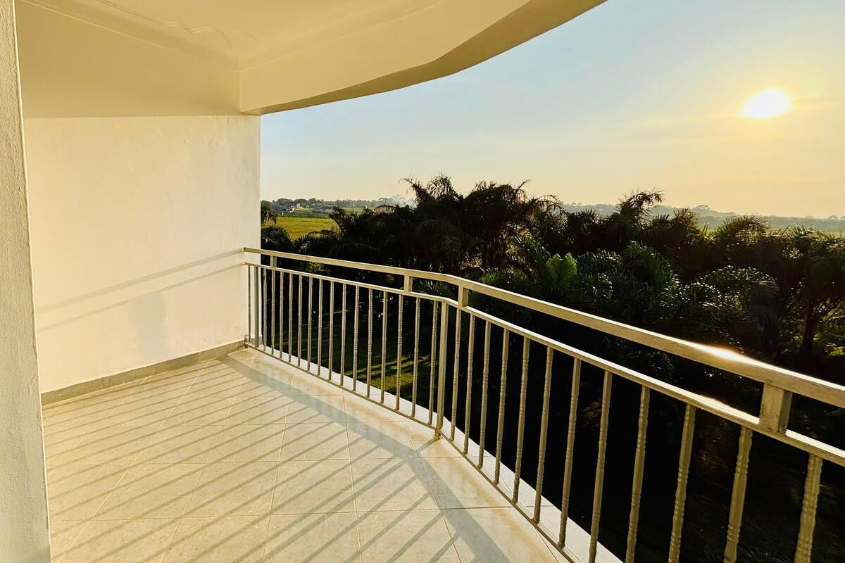 A balcony with a tiled floor and metal railing, overlooking a landscape with trees and a distant view of a town.