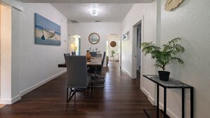 Un couloir comprenant un coin repas, un plancher en bois, une plante en pot et des œuvres d’art accrochées aux murs.