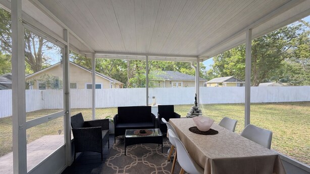 Une terrasse couverte avec une table et des chaises, un tapis et une vue sur le jardin.